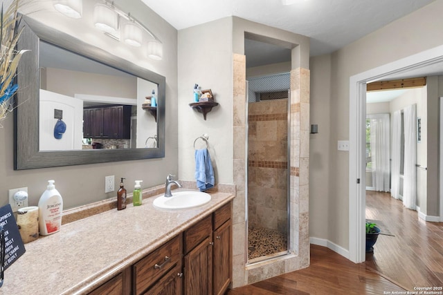 bathroom featuring wood finished floors, a shower stall, vanity, and baseboards