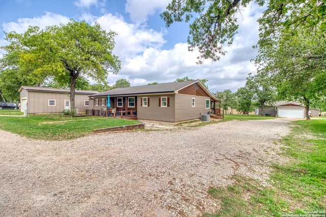 view of front of home featuring a front yard, a garage, central AC unit, an outbuilding, and covered porch