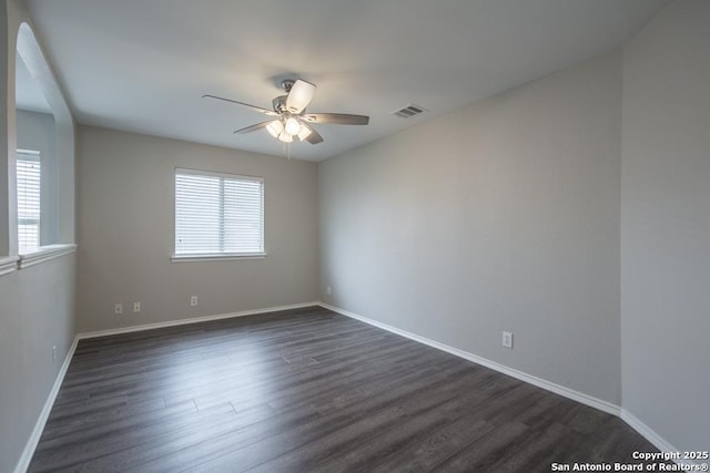spare room with dark wood-type flooring, ceiling fan, visible vents, and baseboards