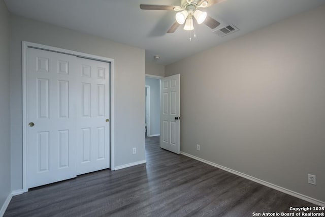 unfurnished bedroom with dark wood-style floors, visible vents, a closet, and baseboards