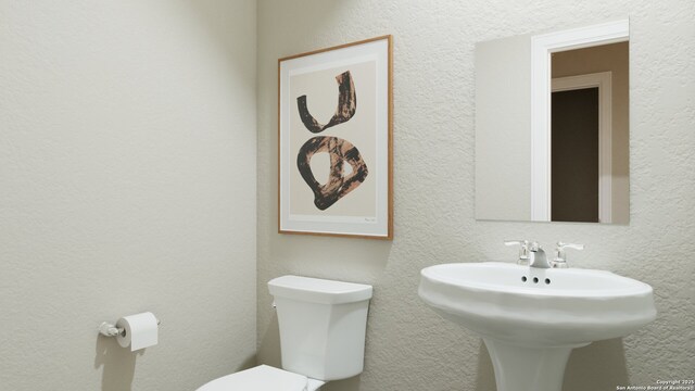half bath featuring toilet, a textured wall, and a sink