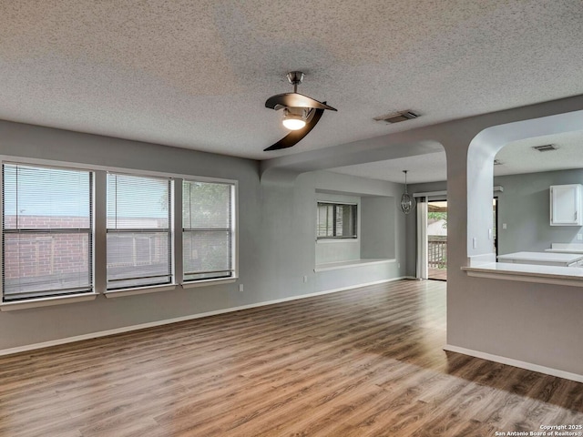 unfurnished living room featuring a textured ceiling, visible vents, baseboards, wood finished floors, and a ceiling fan