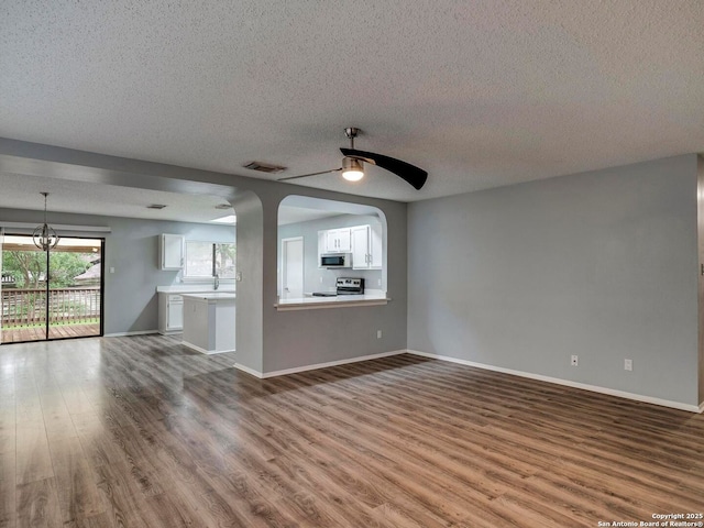 unfurnished living room with a textured ceiling, visible vents, baseboards, wood finished floors, and ceiling fan with notable chandelier