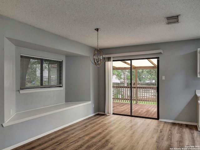 unfurnished dining area with a textured ceiling, a healthy amount of sunlight, wood finished floors, and visible vents