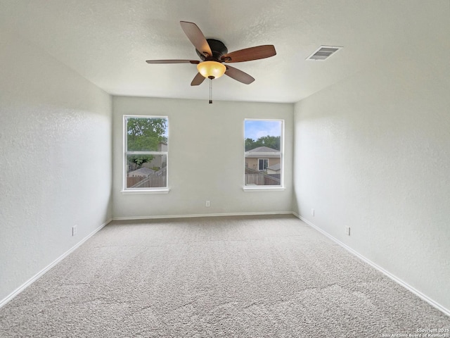 carpeted spare room featuring baseboards, visible vents, a ceiling fan, and plenty of natural light