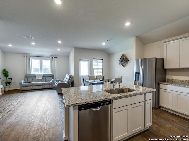 kitchen featuring stainless steel appliances, a sink, open floor plan, dark wood-type flooring, and a center island with sink