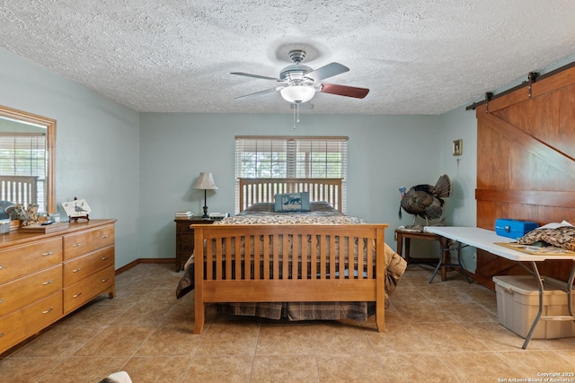 bedroom with a barn door, light tile patterned floors, baseboards, a ceiling fan, and a textured ceiling