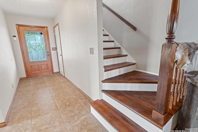tiled entrance foyer featuring a textured ceiling, stairs, and baseboards
