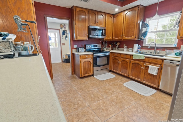 kitchen with appliances with stainless steel finishes, light countertops, brown cabinetry, and a sink