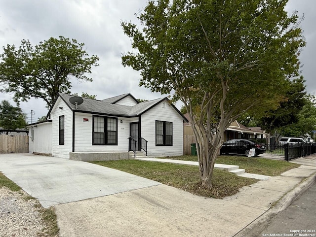 view of front of home featuring a front lawn, fence, a shingled roof, and concrete driveway