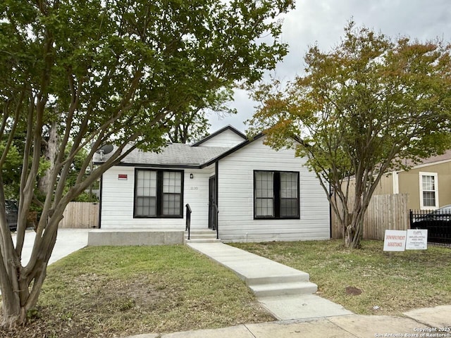 view of front facade with fence, roof with shingles, and a front lawn
