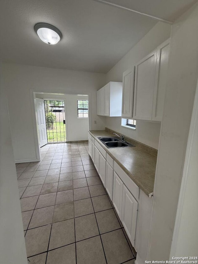 kitchen with white cabinetry, a sink, light countertops, baseboards, and light tile patterned flooring