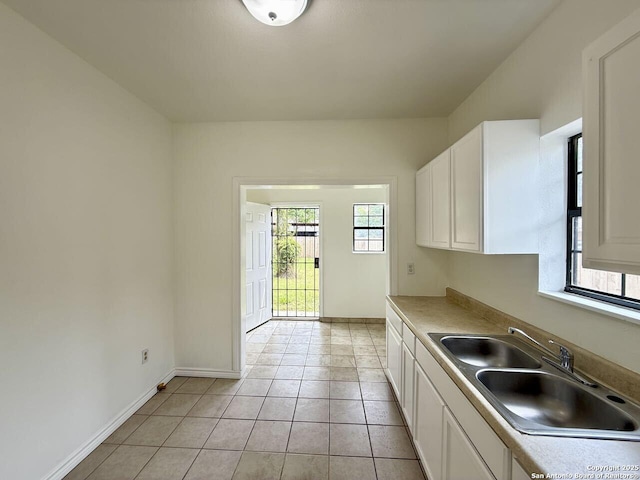 kitchen with light tile patterned floors, white cabinets, a sink, light countertops, and baseboards