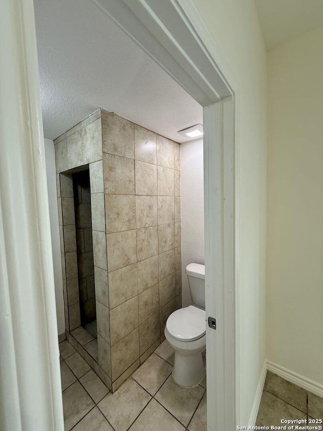 bathroom featuring a textured ceiling, toilet, tile patterned flooring, and tiled shower