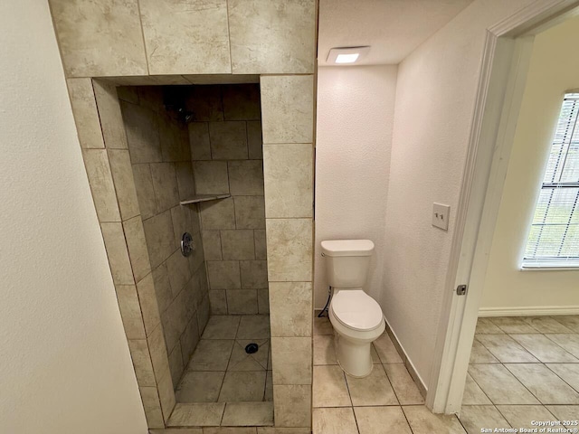 bathroom with a tile shower, toilet, and tile patterned flooring