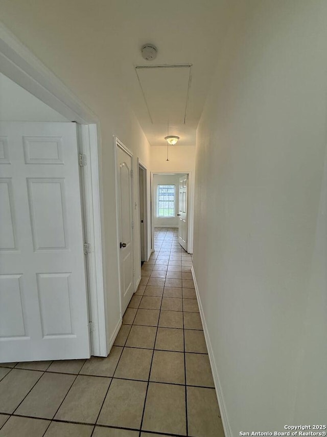 hallway with baseboards, light tile patterned floors, and attic access