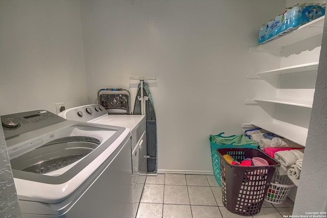 clothes washing area with light tile patterned floors, washer and dryer, laundry area, and baseboards