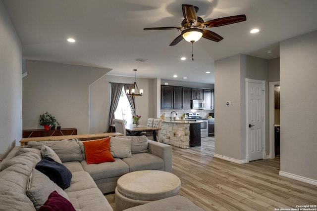 living room featuring light wood finished floors, recessed lighting, visible vents, baseboards, and ceiling fan with notable chandelier