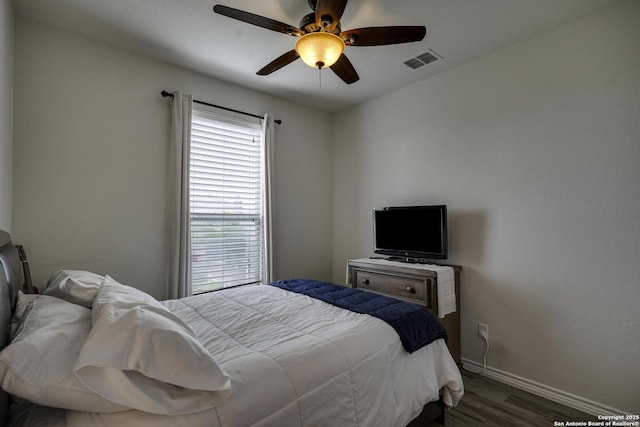 bedroom featuring baseboards, visible vents, wood finished floors, and multiple windows