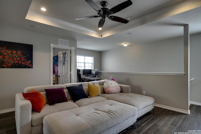 living area with crown molding, a tray ceiling, baseboards, dark wood-type flooring, and a ceiling fan