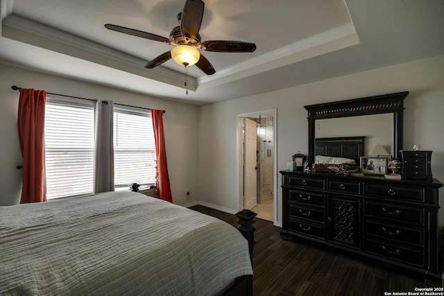 bedroom featuring connected bathroom, dark wood-type flooring, baseboards, crown molding, and a tray ceiling