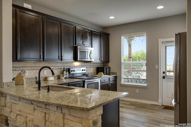 kitchen featuring a sink, stainless steel appliances, light wood-type flooring, light stone countertops, and backsplash