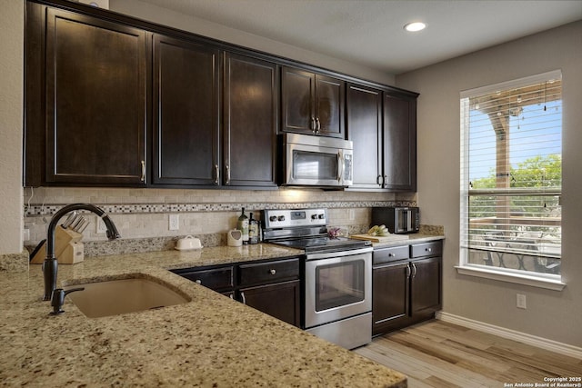 kitchen featuring stainless steel appliances, light wood-style floors, decorative backsplash, and a sink