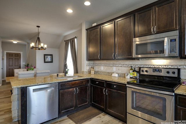 kitchen with a sink, a chandelier, stainless steel appliances, light wood-style floors, and a peninsula