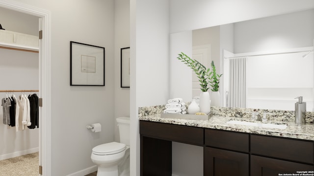 bathroom with toilet, a walk in closet, vanity, and baseboards