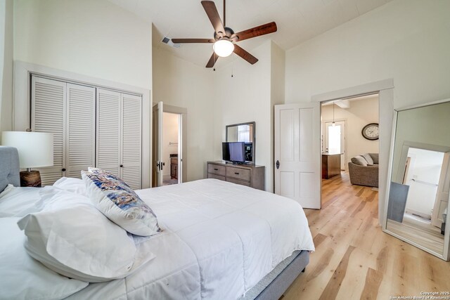bedroom featuring high vaulted ceiling, ceiling fan, light wood-style floors, and a closet