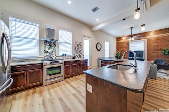 kitchen with wall chimney range hood, a sink, appliances with stainless steel finishes, visible vents, and light wood-style floors