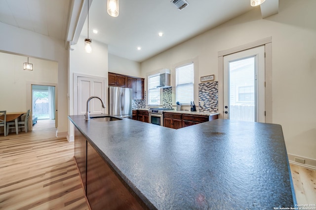 kitchen featuring stainless steel appliances, light wood-style floors, wall chimney range hood, a sink, and visible vents