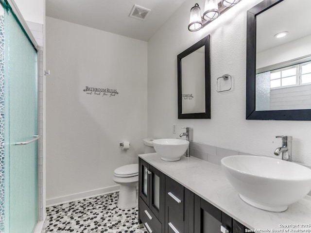 bathroom with baseboards, visible vents, a shower with shower door, and a sink