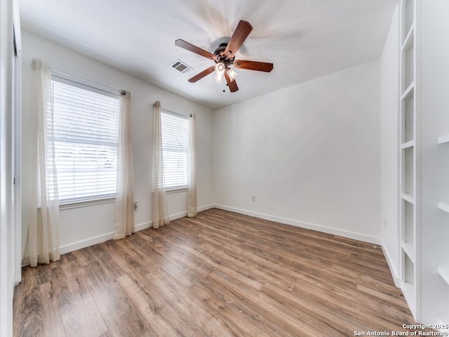 empty room with visible vents, a ceiling fan, light wood-style flooring, and baseboards