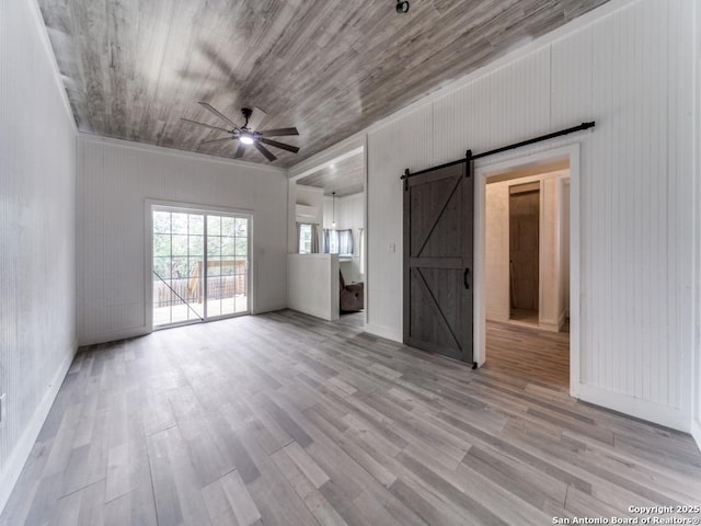 unfurnished living room featuring a barn door, wood finished floors, and a ceiling fan