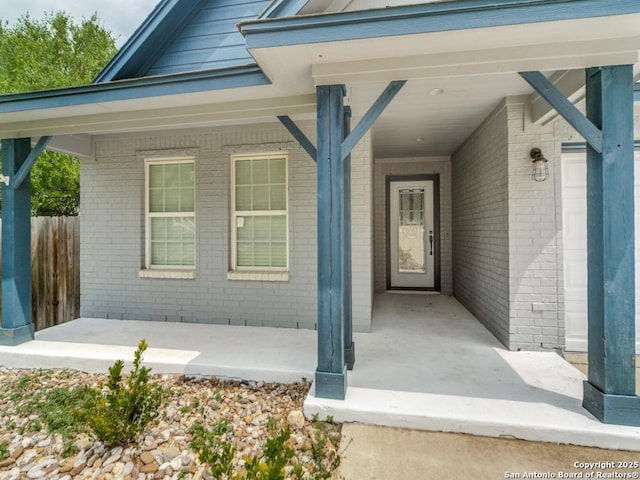 view of exterior entry featuring fence, a porch, and brick siding