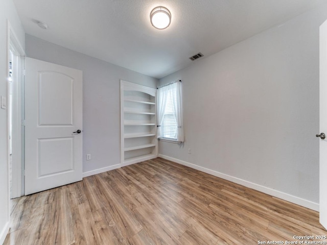 empty room with visible vents, built in shelves, light wood-style flooring, and baseboards