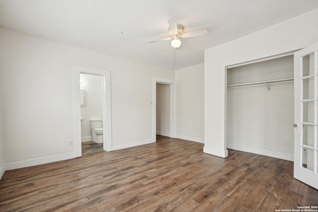 unfurnished bedroom with wood finished floors, ensuite bath, a closet, baseboards, and a ceiling fan