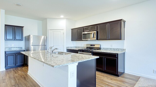 13406 Flower Pond, Saint Hedwig, TX 78152 - kitchen with light stone counters, light wood-style flooring, a sink, appliances with stainless steel finishes, and a kitchen island with sink