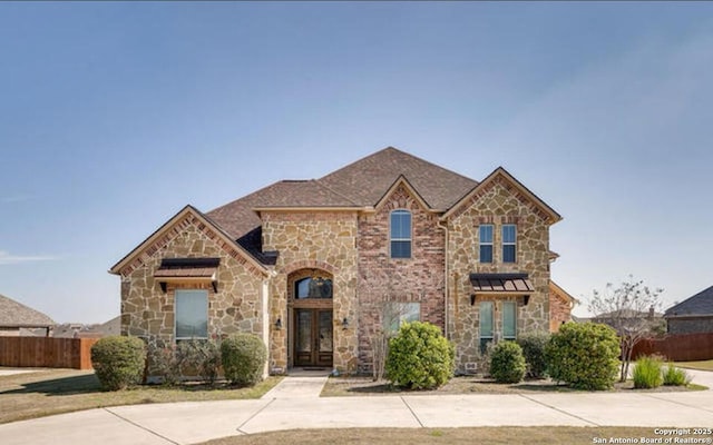 view of front of property featuring fence, french doors, and stone siding