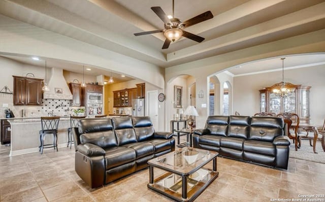 living area with arched walkways, ceiling fan with notable chandelier, and a raised ceiling