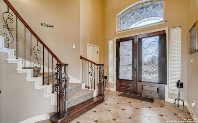 foyer entrance with a high ceiling, stairway, french doors, and baseboards