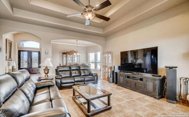 living room with arched walkways, ceiling fan with notable chandelier, a wealth of natural light, and a tray ceiling