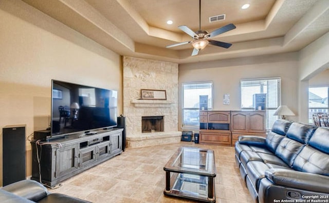 living room featuring plenty of natural light, a fireplace, visible vents, a raised ceiling, and a ceiling fan