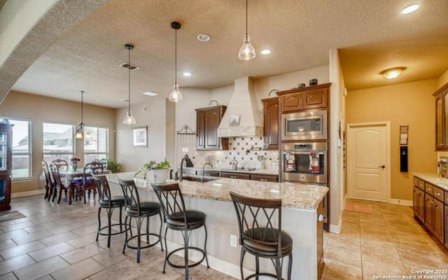 kitchen featuring appliances with stainless steel finishes, a textured ceiling, premium range hood, and a sink