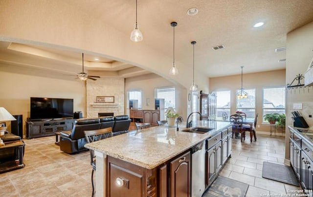 kitchen with light stone counters, a sink, a breakfast bar, dishwasher, and a ceiling fan