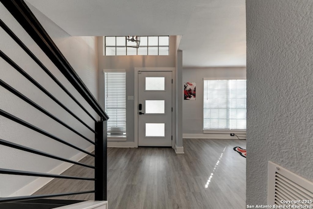 entrance foyer with wood finished floors, stairs, a textured wall, baseboards, and a notable chandelier