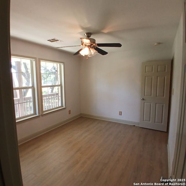 empty room featuring a ceiling fan, visible vents, light wood-style flooring, and baseboards
