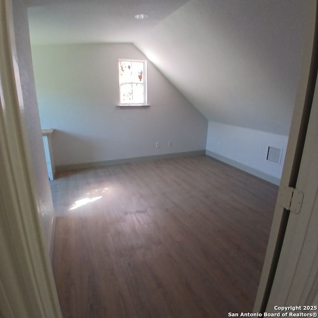 additional living space featuring wood finished floors, visible vents, vaulted ceiling, and baseboards