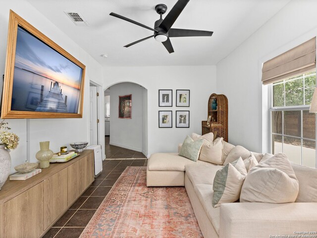 living area with arched walkways, ceiling fan, visible vents, and dark tile patterned flooring